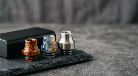 Composizione elegante di drip tip artigianali in legno stabilizzato, resina e metallo disposti su una superficie minimalista